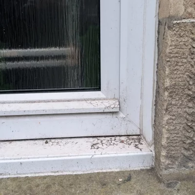Initial stage of window frame preparation, showing scraping or stripping work to remove old, damaged sealant and paint before applying new finishes.